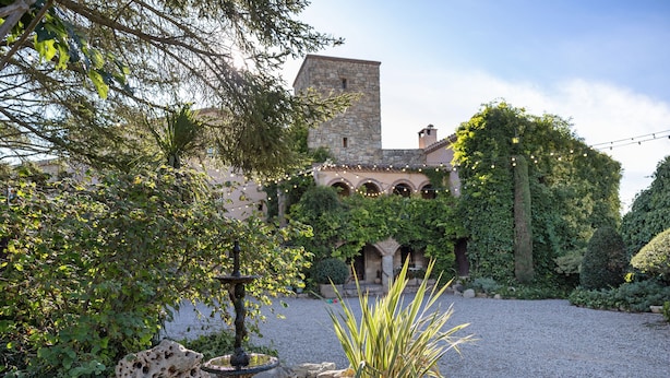 A courtyard with a fountain, a stone wall, and a building with arched windows and ivy.