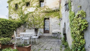 A stone building with ivy-covered walls, a courtyard with a table and chairs, and a door.