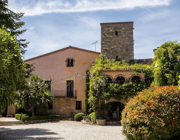 Un bâtiment doté d’une tour en pierre, d’une cour et d’un jardin où poussent différentes espèces de plantes.
