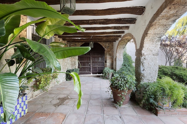 A courtyard with stone flooring, wooden beams, and potted plants.