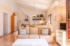 A living room with a sofa, a coffee table, a TV, a lamp, and a kitchen in the background.