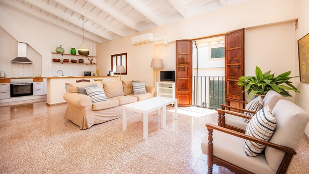 A spacious living area with a kitchen, a sofa, a coffee table, and a wooden chair. - Apartment 'Can Claret' with Balcony, Wi-Fi and Air Conditioning (Felanitx)