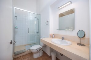 Ein Badezimmer mit Duschkabine aus Glas, Toilette, Waschbecken und Spiegel.