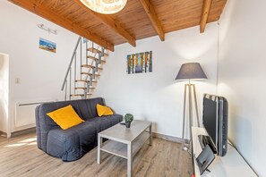 A modern living room with a grey sofa, a small table, a lamp, a TV, and a staircase.