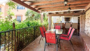 An outdoor patio with a table and chairs, a railing, and a view of a building with a brick wall and a window. - Casa del Golf – 15-min walk to the beach, mountain view, private pool, Wi-Fi (Málaga)