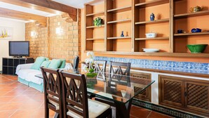 A dining area with a glass table, wooden chairs, a brick wall, and a tiled backsplash. - Casa del Golf – 15-min walk to the beach, mountain view, private pool, Wi-Fi (Málaga)