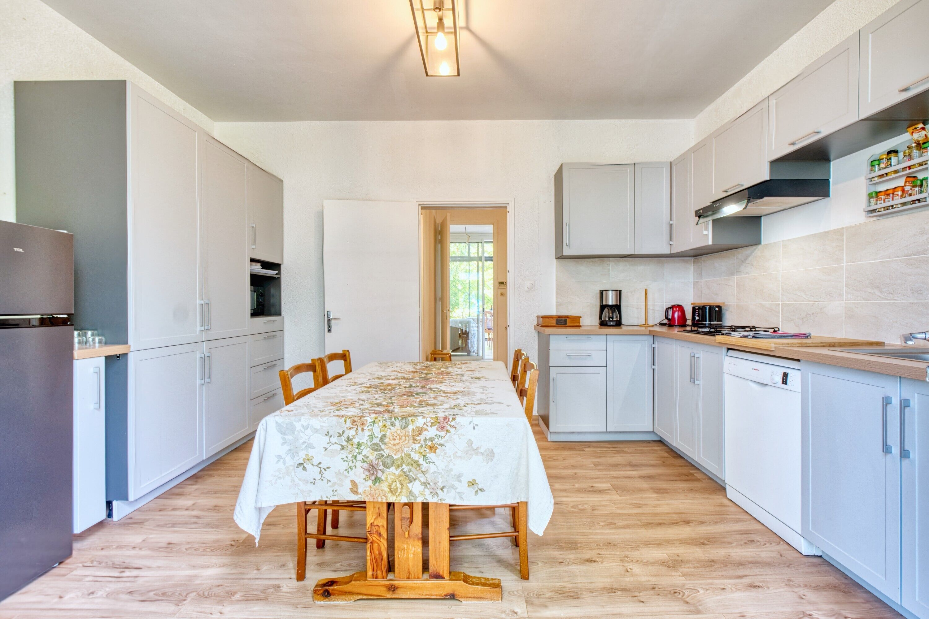 Une cuisine moderne avec des meubles blancs, une table à manger en bois et une vue sur l’espace repas.