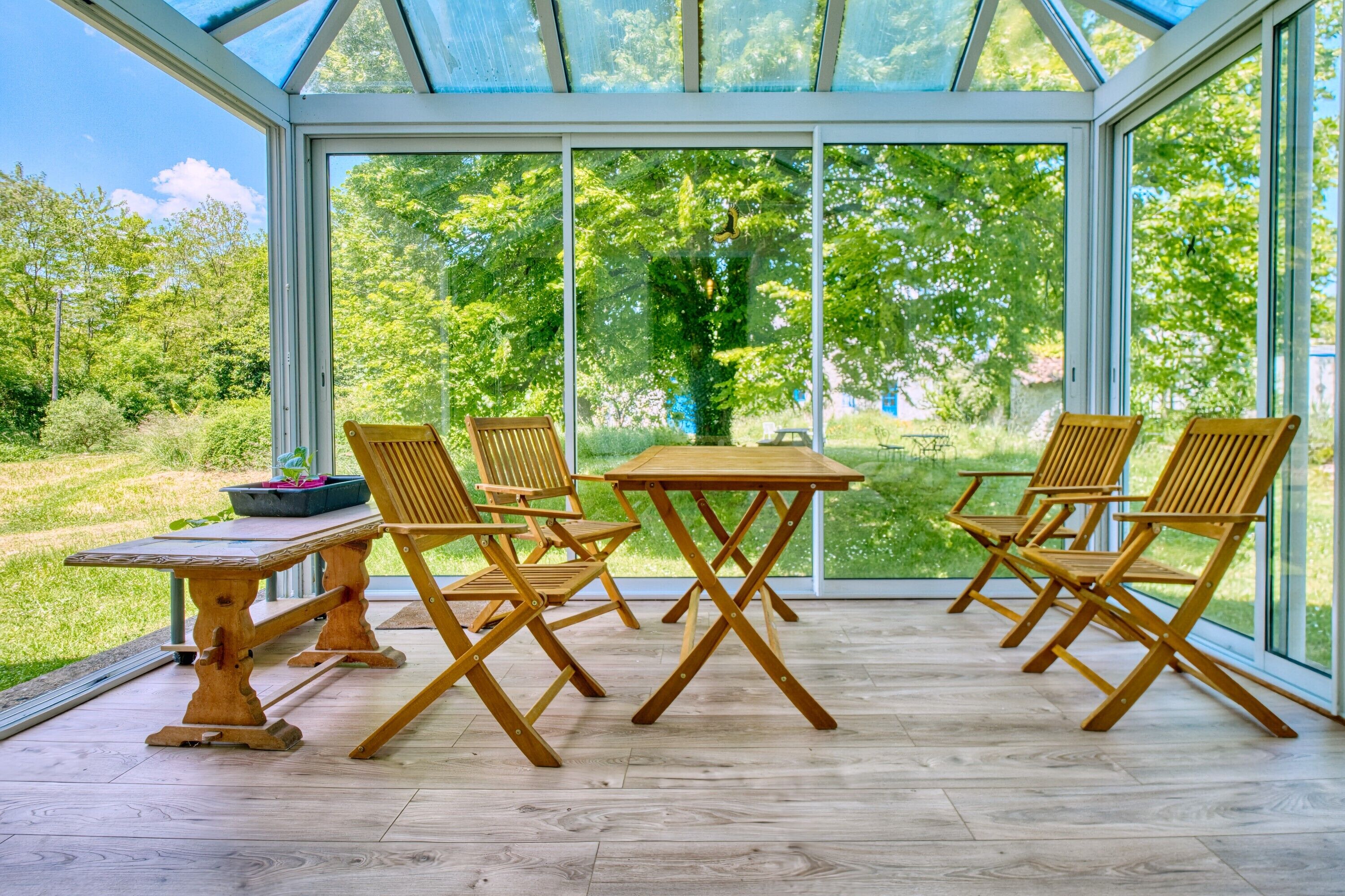 Una veranda con tavolo e sedie in legno, ampie vetrate e vista sul verde.