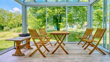 Una veranda con tavolo e sedie in legno, ampie vetrate e vista sul verde.