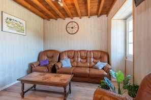 Une pièce avec un plafond en bois, un canapé en cuir marron agrémenté de coussins, une table basse en bois et une horloge murale.
