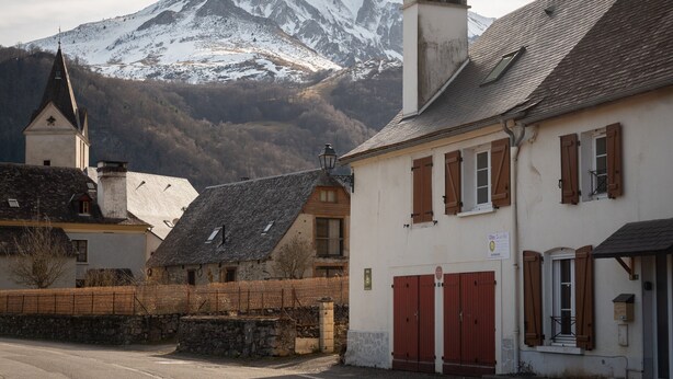 Un edificio con puerta roja, pared de piedra y montaña al fondo.