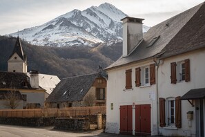 Un edificio con puerta roja, pared de piedra y montaña al fondo.