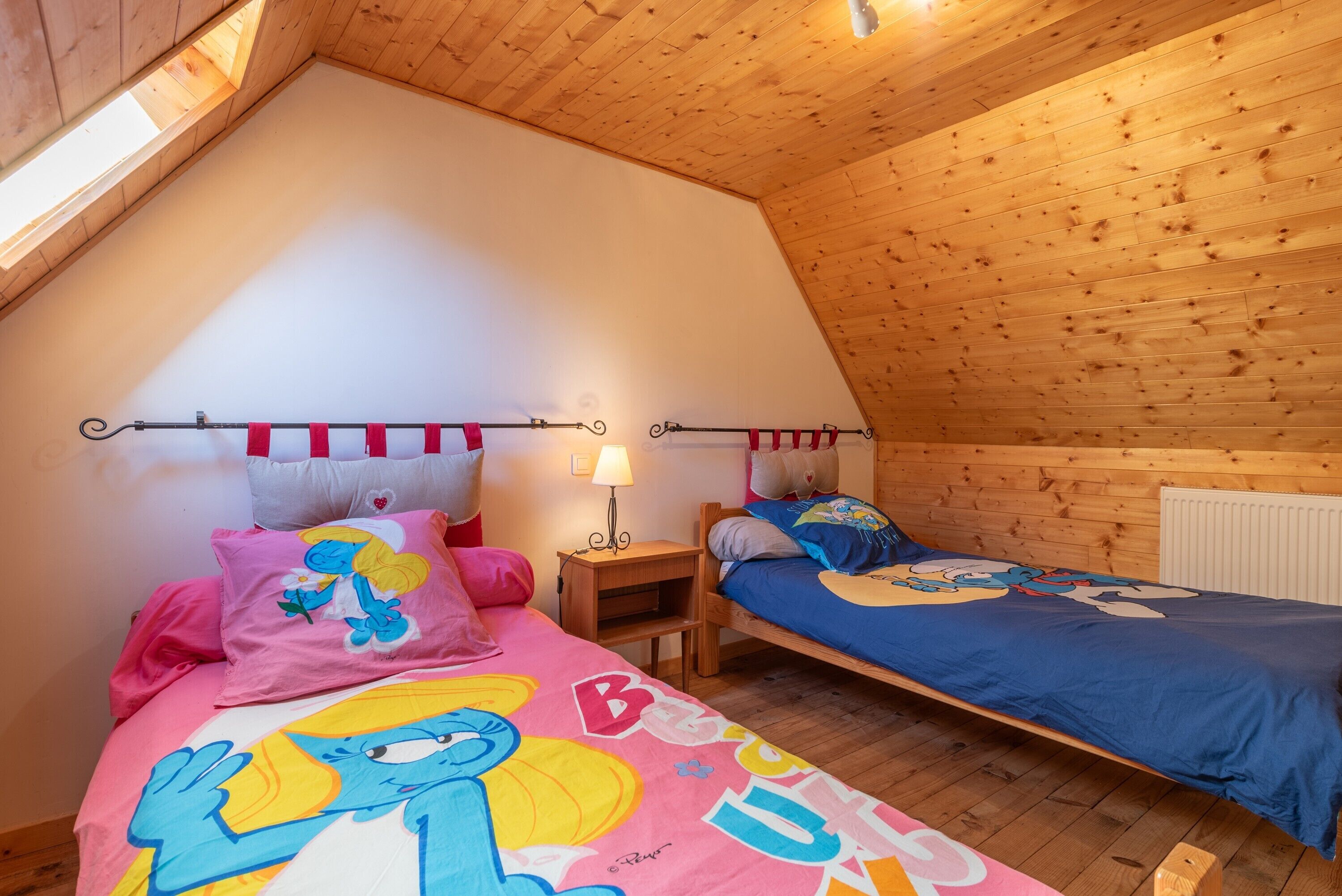 Ein gemütliches Schlafzimmer im Dachgeschoss mit zwei Betten, Holzwänden, einer geneigten Decke und einem Oberlicht.