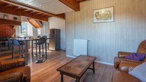 Amplia sala de estar con techo de madera, mesa de comedor con sillas, sofá de cuero y cocina al fondo.