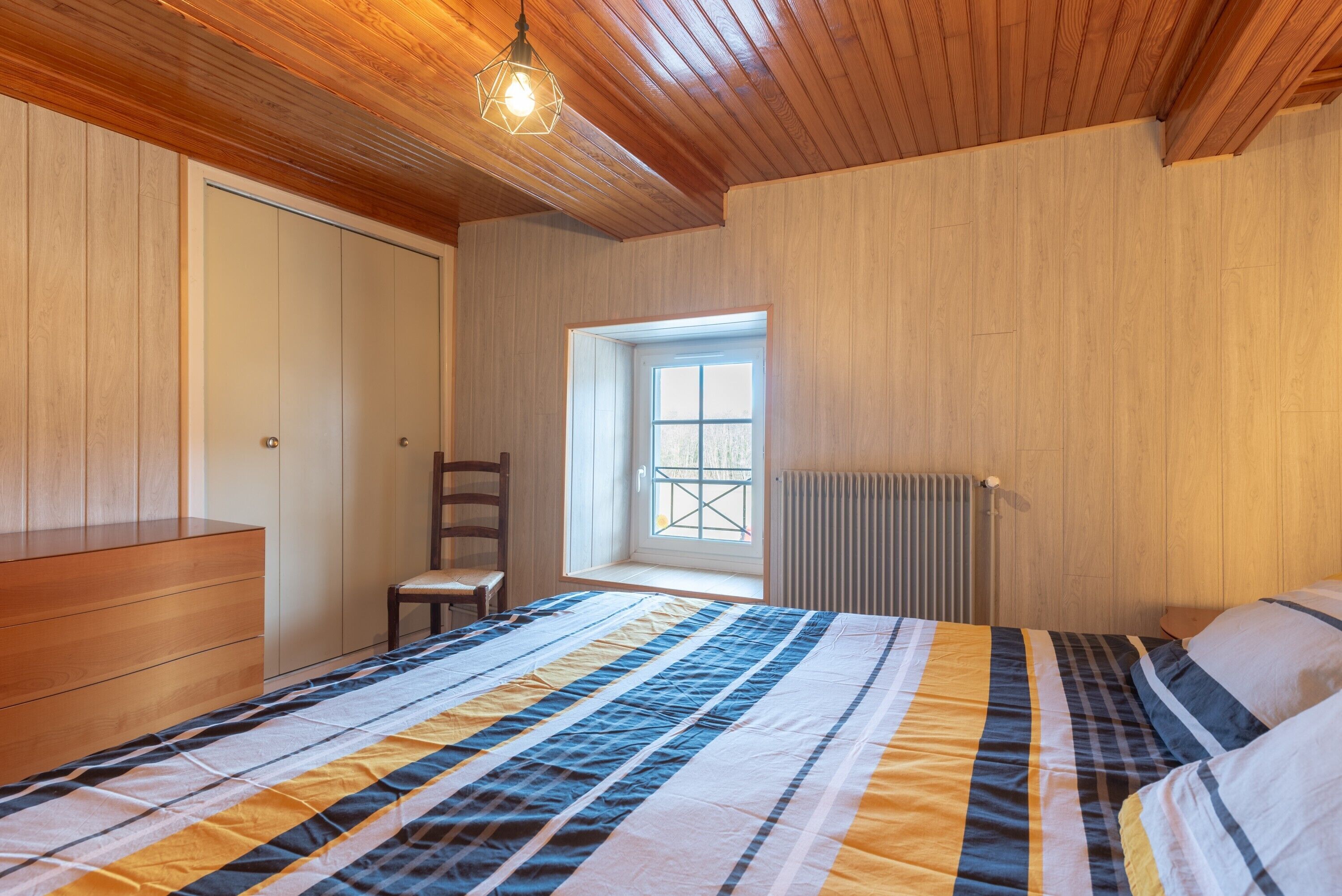 A bedroom with a bed, a wooden dresser, a chair, a window, and a radiator.