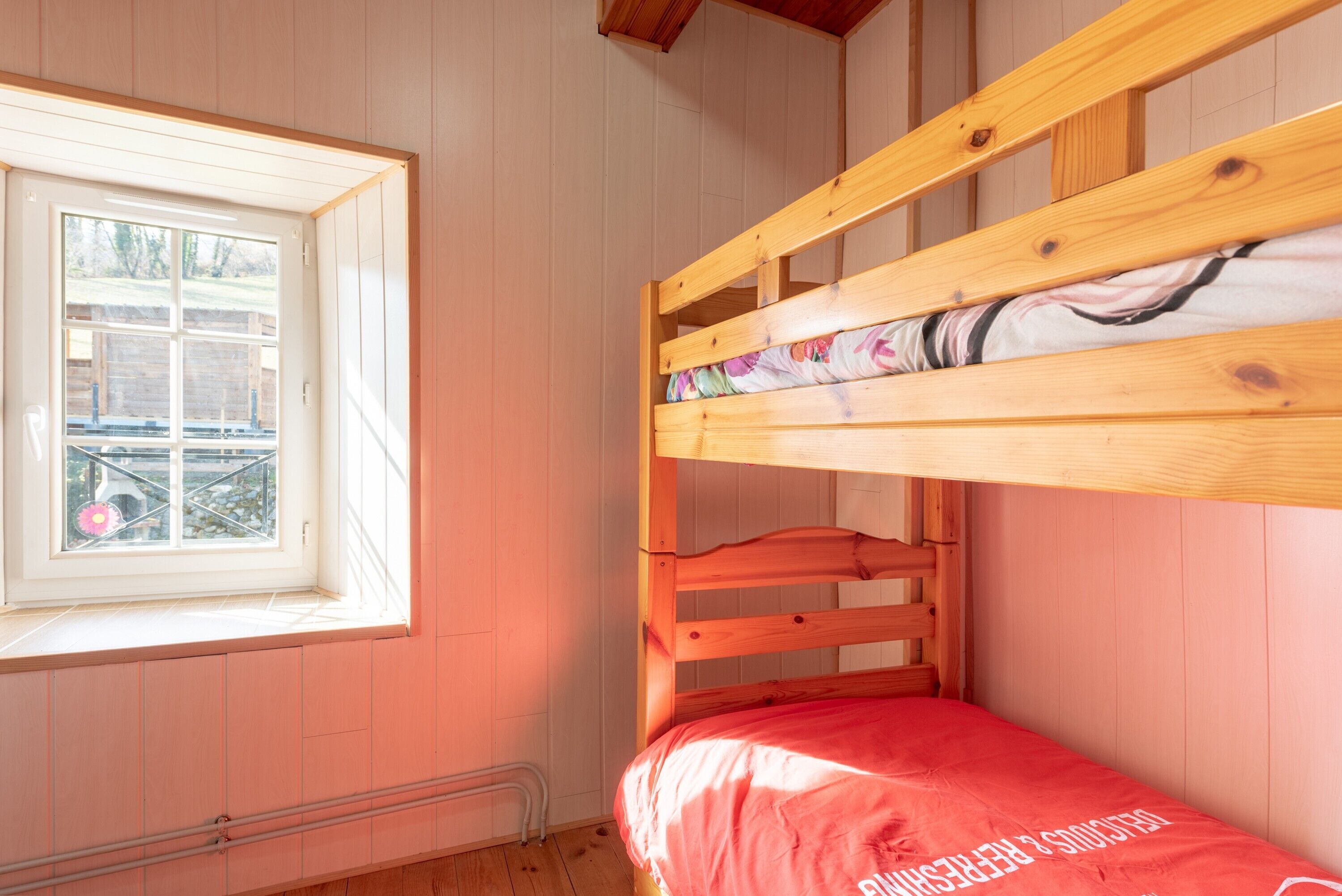 A bunk bed with a window, wooden walls, and a radiator.