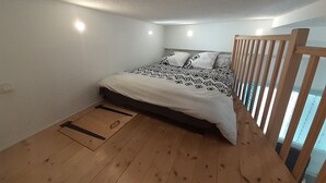 Une chambre avec un plancher en bois, un lit avec une literie à motifs, une tête de lit et une fenêtre avec des stores.