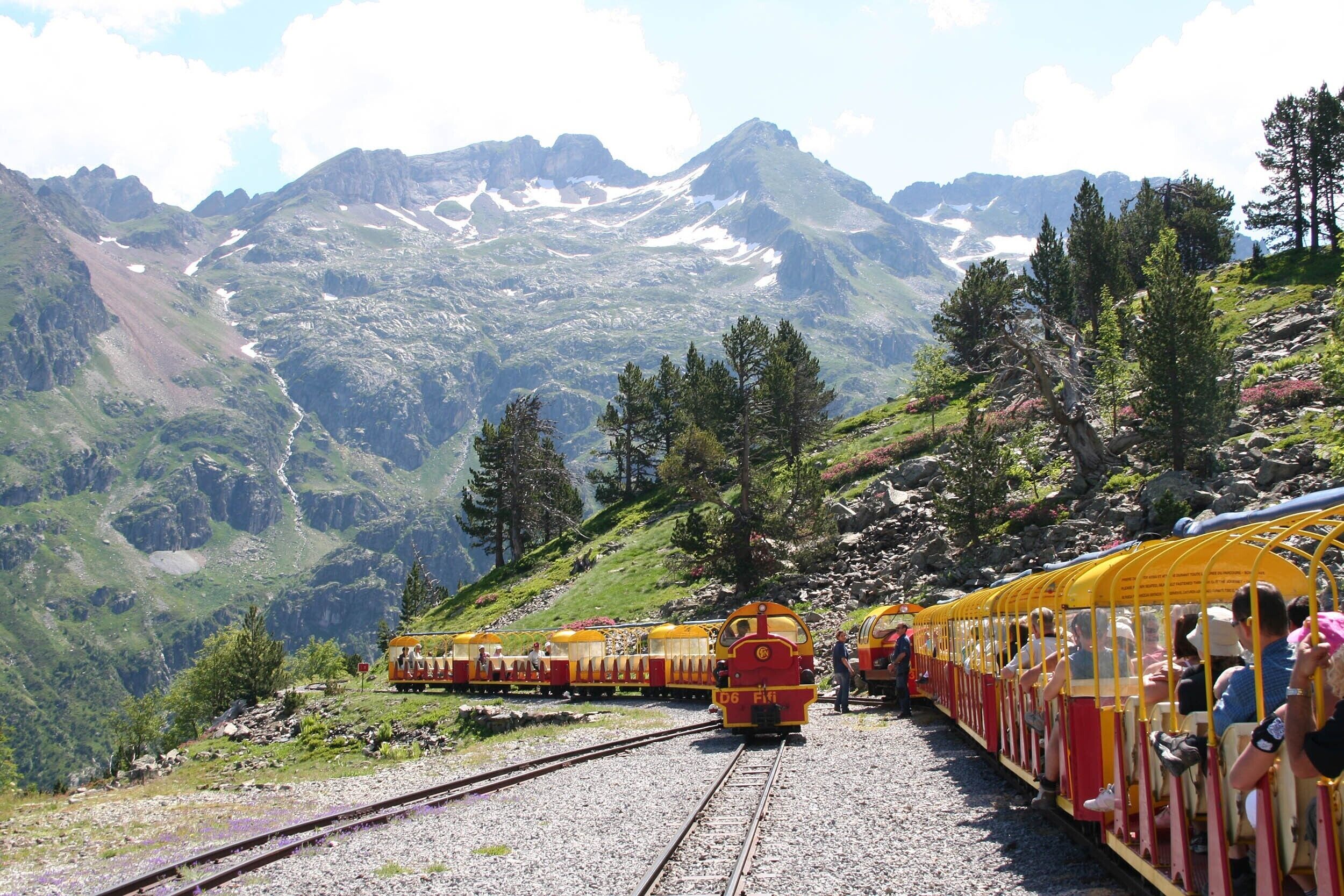 Un tren de montaña con pasajeros, vías y un paisaje montañoso.