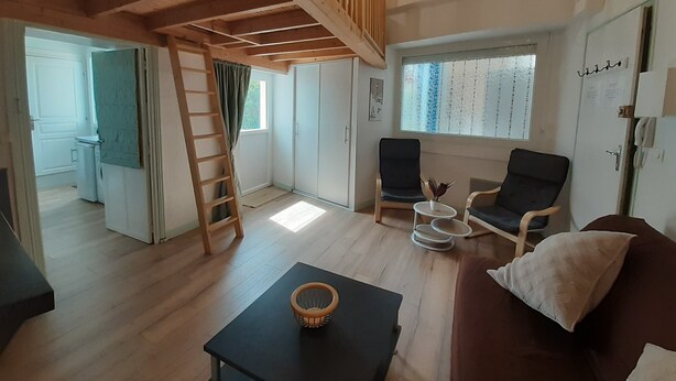 Une pièce avec un lit en mezzanine, un bureau, deux chaises, une petite table et une fenêtre avec des rideaux.