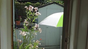 Une porte-fenêtre donnant sur un patio où se trouvent un pot de fleurs, un étendoir et, au fond, un abri de jardin.