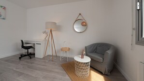 Una camera moderna con scrivania, sedia, lampada, specchio rotondo e un divano grigio.