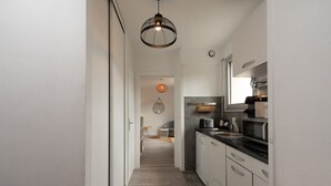 Un corridoio stretto che porta a una cucina con mobili bianchi, un forno a microonde e un lampadario.
