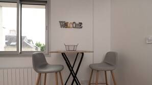 Una stanza con un tavolo, due sedie, una finestra e un cartello con la scritta 'WELCOME' appeso al muro.