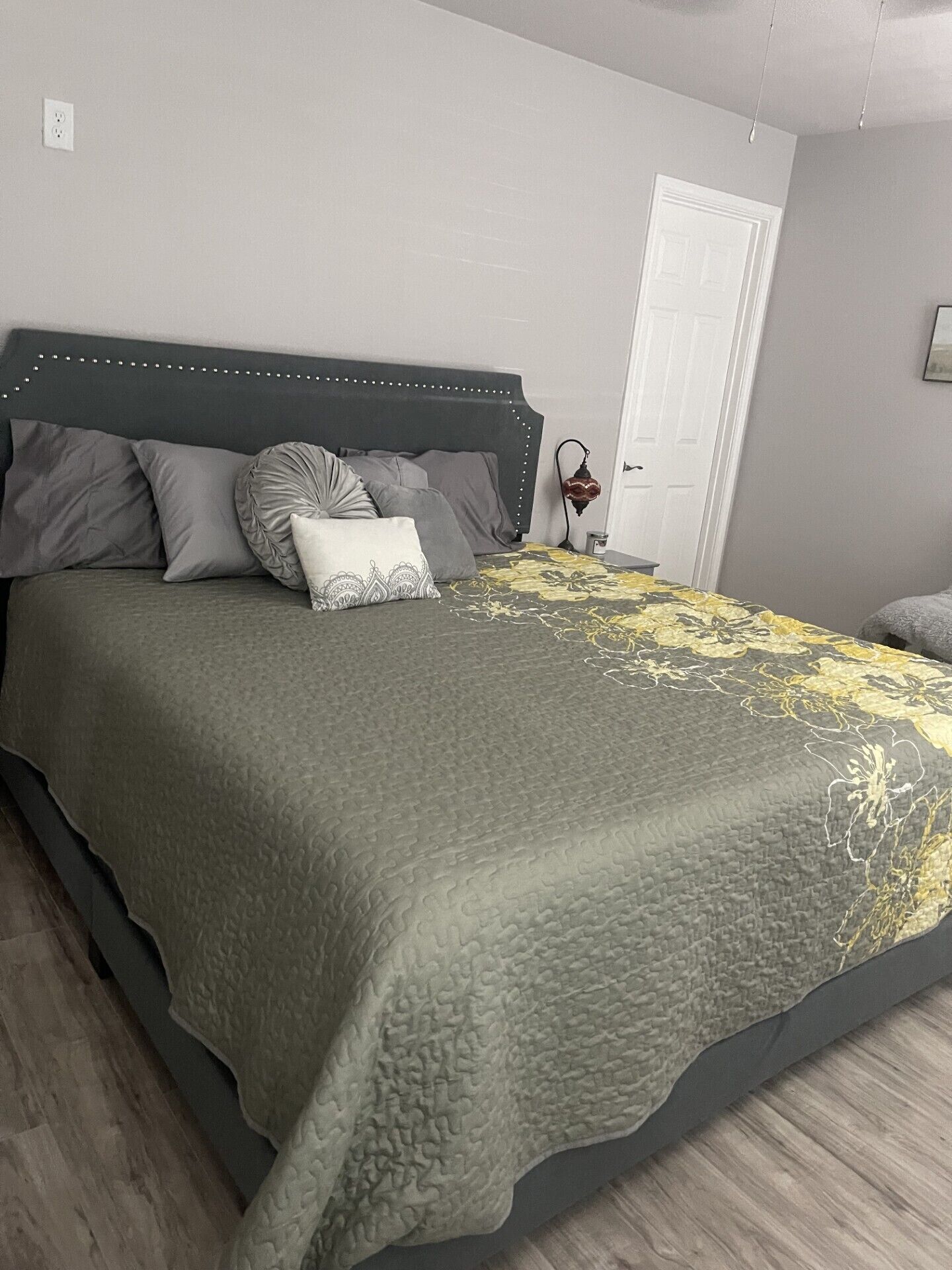 Ein Schlafzimmer mit einem Bett, Kissen, einem Nachttisch, einer Lampe und einer Tür.