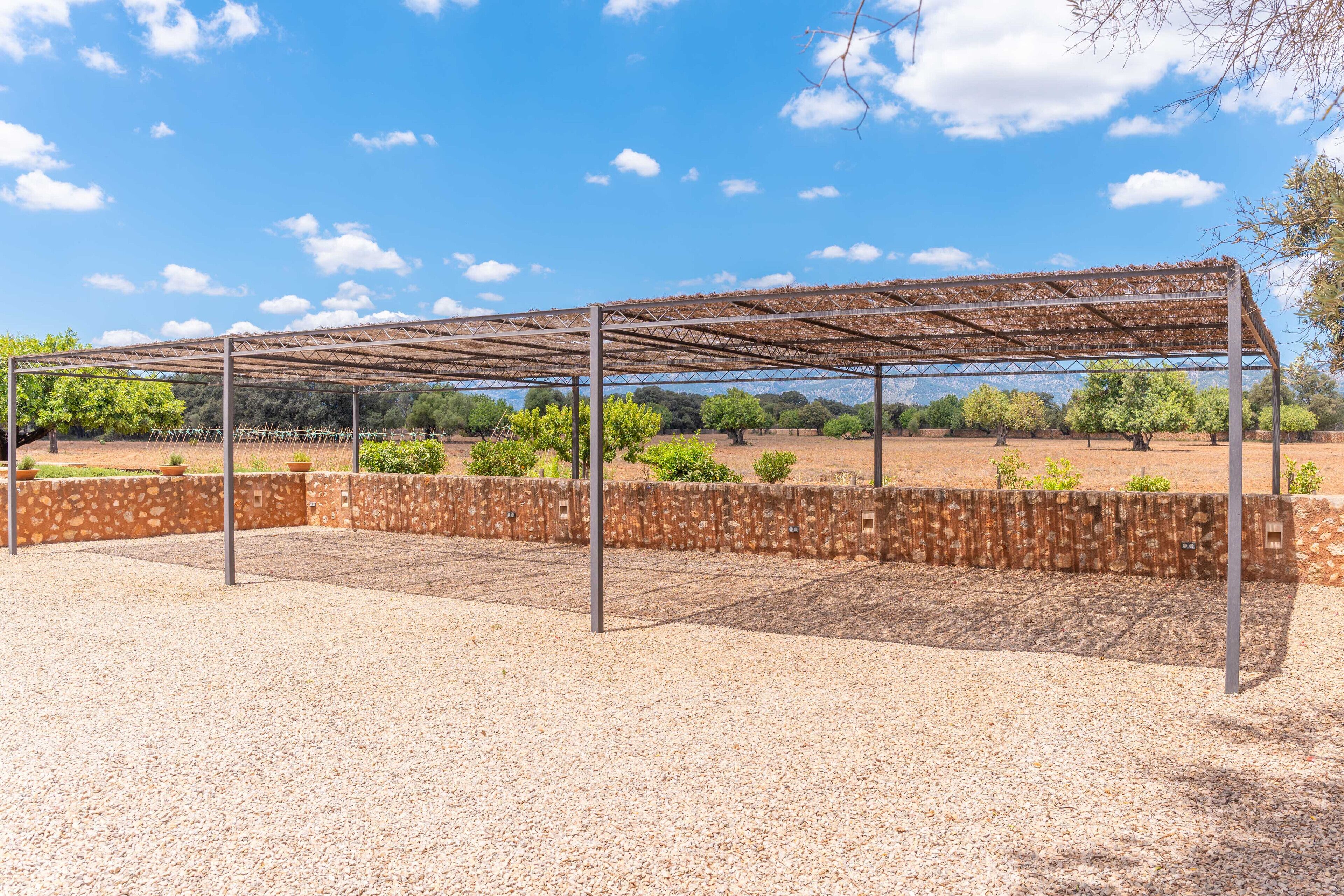 Un espace extérieur abrité, doté d’un sol en gravier et de murs en pierre, entouré d’arbres et surplombé d’un ciel dégagé.