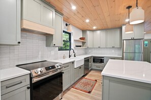 A modern kitchen with white cabinetry, stainless steel appliances, and a wooden ceiling. - The Redhawk | Hocking Hills, Sauna, EV Charger (Logan)