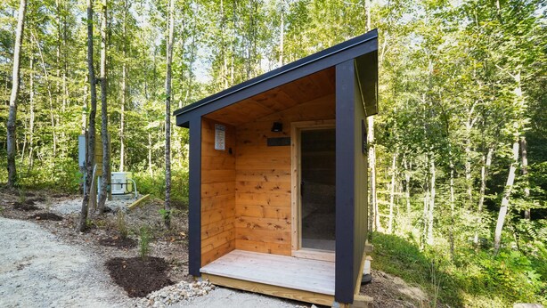 Uma pequena cabana de madeira com porta e janela, cercada por árvores.