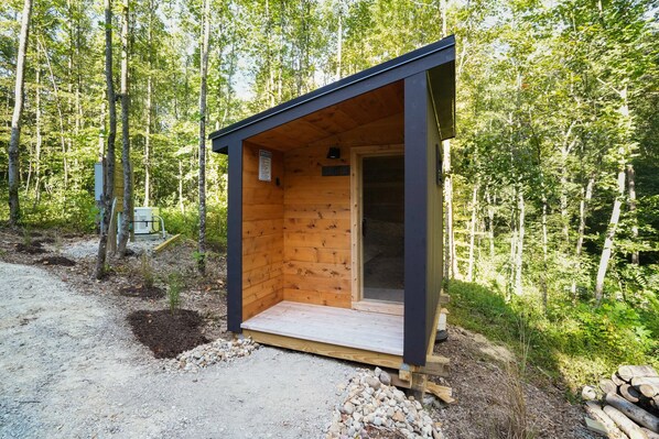 A small wooden cabin with a door and a window, surrounded by trees.