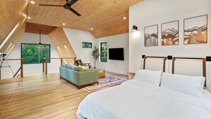 Quarto com uma cama grande, ventilador de teto, piso de madeira, televisão e obras de arte na parede.