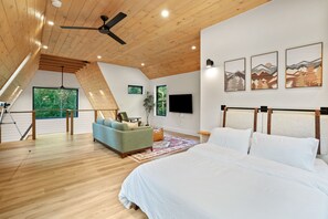 A bedroom with a large bed, a ceiling fan, wooden floors, a TV, and artwork on the wall.