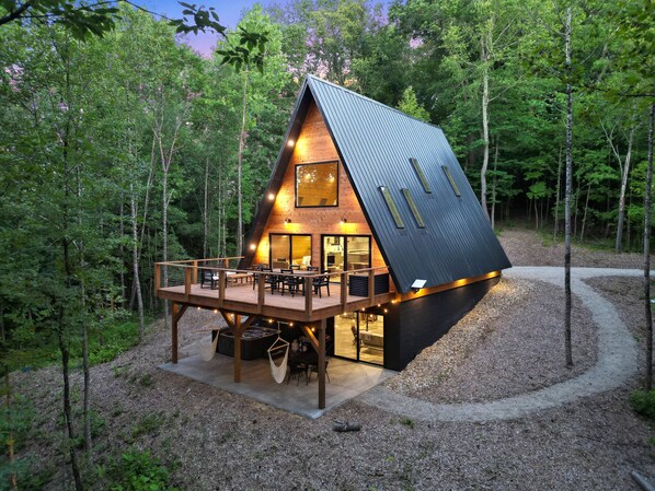 A modern cabin with a sloped roof, wooden deck, and a fire pit area.
