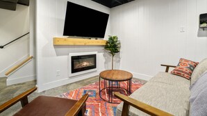 Uma sala de estar acolhedora com lareira, uma TV de tela plana na parede, um sofá confortável e um banco de madeira.