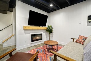 A cozy living room with a fireplace, a flat-screen TV mounted on the wall, a comfortable sofa, and a wooden bench.