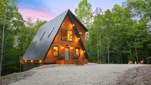 A modern log cabin with a sloped roof, a wooden deck, and a gravel driveway.