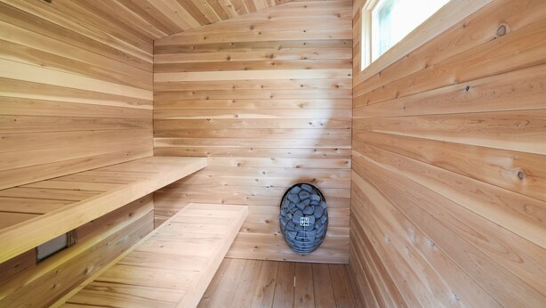 A wooden sauna with slatted walls, a bench, and a stone heater.