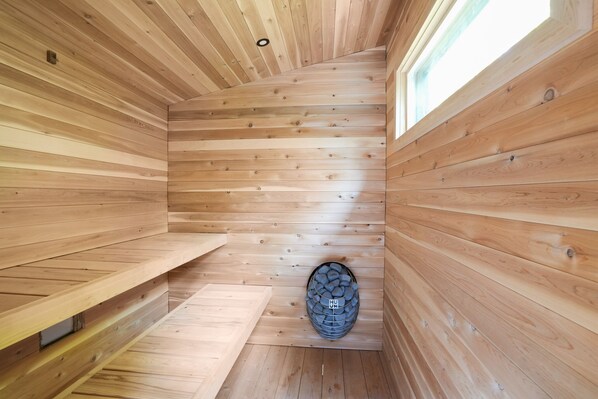 Un sauna en bois avec des parois à lattes, un banc et un poêle en pierre.