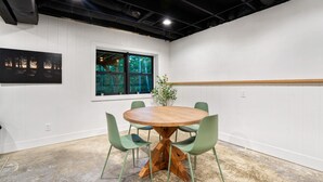 Uma sala de conferências com uma mesa redonda de madeira, cadeiras verdes, um vaso de plantas e uma janela com vista para árvores.