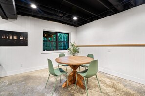 A conference room with a round wooden table, green chairs, a potted plant, and a window with a view of trees.