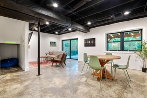 A spacious room with a high ceiling, a dining area with a round wooden table and chairs, a sofa, and a large window with a view of trees. - The Redhawk | Hocking Hills, Sauna, EV Charger (Logan)