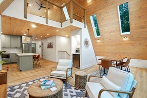 A spacious living area with a high ceiling, wooden beams, and large windows.
