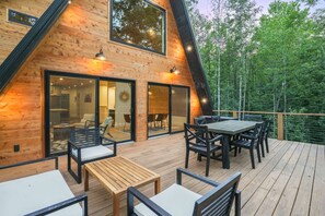 A wooden cabin with a deck, outdoor seating, and large windows.