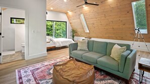 A modern interior with a green sofa, a wooden ceiling, and a large window offering a view of greenery.