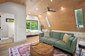 Un intérieur moderne avec un canapé vert, un plafond en bois et une grande fenêtre donnant sur un paysage verdoyant.