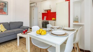 Un salon moderne avec un canapé gris, une table à manger dressée avec des assiettes et des verres, et une cuisine dont le mur du fond est recouvert de carreaux rouges.