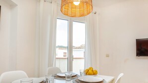 Un coin repas avec une table dressée pour quatre personnes, une lampe en osier et une vue sur l’extérieur par une fenêtre.