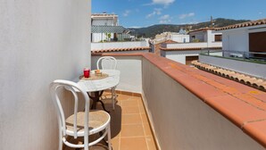 Un balcon avec une table et des chaises blanches, une tasse rouge et un petit gâteau sur la table.